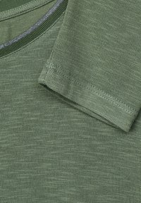 Green knit fabric with a smooth texture, featuring a crew neckline and short sleeves. Notable stitching detail near the collar.