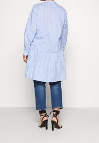 Blauw-wit gestreepte shirt met een geplooide zoom, gecombineerd met lichtblauwe jeans en zwarte sandalen met hoge hakken en banden.