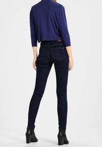 Tummansiniset korkeavyötäröiset kapeat farkut, joissa takataskut ja ompeludetaljit. Yhdistetty lyhyeen laivastonsiniseen toppiin ja mustiin nilkkureihin.