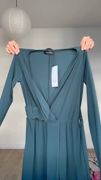 Čajnozelena, dugačka haljina na preklop s dugim rukavima i remenom, drži se rukama u prostoriji s drvenim podom i bijelim papirnatim lampionom na stropu.