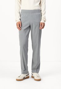 Pantalons gris légers avec une taille élastique, présentant une texture subtile. Associés à un haut à manches longues de couleur crème et des sneakers blanches.