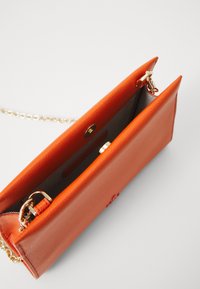 Borsa a mano in pelle arancione con una finitura texturizzata, dotata di una tracolla in catena dorata, chiusura sicura e una tasca interna, parzialmente aperta.