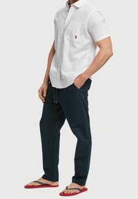 Bílá lněná košile s krátkým rukávem a kapesníčkem, kombinovaná s tmavými kalhotami a červenými žabkami s námořnickýma páskami.