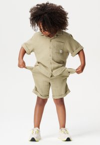 Chemise en coton beige clair à manches courtes et shorts assortis, avec une poche et des poignets retroussés, en tissu texturé et coupe décontractée.