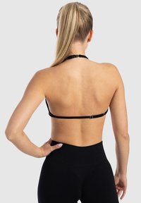 Zwarte halter bralette van soepel materiaal, met een smalle band aan de achterkant en een veilige haaksluiting.