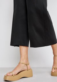 Beige plattform sandaler med en kraftig sula, öppen tå och tunna ankelremmar. Skon har en slät, matt yta.