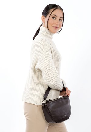 Brown leather handbag with a curved shape, silver hardware, and a short strap, held by a person wearing a cream knit turtleneck sweater.