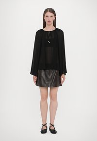 Black sheer top with wide sleeves, layered over a brown leather skirt. Black flats with polka dot pattern complete the outfit.