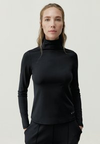 Camiseta negra de manga larga y cuello alto, hecha de una tela suave y elástica. Presenta una silueta ajustada y sutiles detalles cerca del dobladillo.