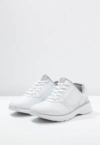 White athletic shoes with mesh and synthetic upper, textured hexagonal pattern, grey accents, cushioned sole, and white laces.