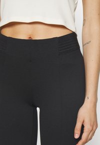 Fekete, magas derekú leggings texturált derékkal, rugalmas anyagból készült. Simaságot és elegáns megjelenést kínál.