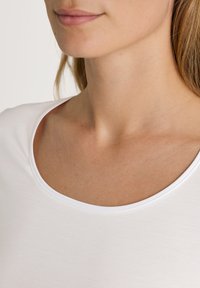 Witte T-shirt met een ronde halslijn, zachte textuur en gladde naden. Close-up weergave van de hals en schoudergebied. Minimalistisch ontwerp.