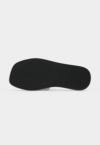 Semelle plate noire de chaussure avec des rainures horizontales subtiles, vue de dessous sur fond blanc.