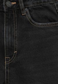 Czarne dżinsy o denimu z kontrastującymi pomarańczowymi szwami, z przednią kieszenią, pętlami na pasek i zapięciem na guziki. Tekstura jest gładka i wytrzymała.