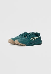 Türkisfarbene Sportschuhe mit einer strukturierten Oberseite, weißen Logoakzenten und einer hellbraunen Gummisohle mit einem gemusterten Profil für Trittsicherheit.