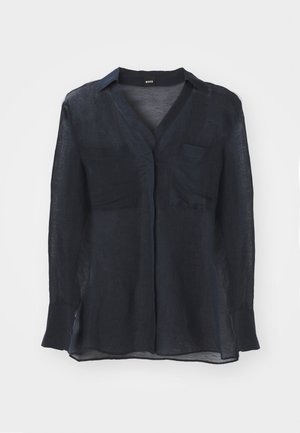 Marineblauwe doorschijnende blouse met lange mouwen en een V-hals, met twee borstzakken en zijsplitten aan de onderkant. Gemaakt van een lichte stof.
