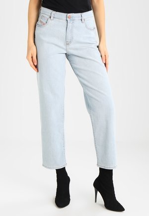 Person wearing light blue straight-leg jeans and black high-heeled ankle boots, standing with arms relaxed by sides.