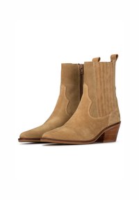 Botas de tobillo de ante en color beige con punteras puntiagudas, que cuentan con una cremallera lateral, detalles de costura vertical y tacones apilados. Textura suave, estilo occidental.