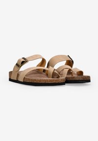 Sandales beiges avec une semelle en liège, dotées de brides croisées, d'une texture lisse et d'un détail de boucle en métal. Design plat adapté à une tenue décontractée.