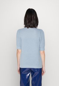 Suéter de punto azul claro con mangas cortas abullonadas, tejido texturizado y puños acanalados. Combinado con pantalones oscuros brillantes.