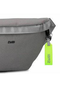 Grijze stoffen tas met een slank ontwerp, voorzien van een omgevouwen bovenkant, zwart logo en een bevestigd felgroen label met tekst.