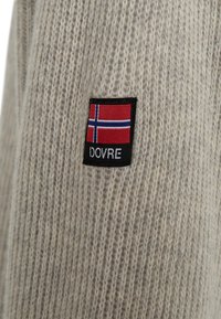 Lys grå strikket sweater med en blød tekstur, der har et sort patch med det norske flagg og teksten "DOVRE".