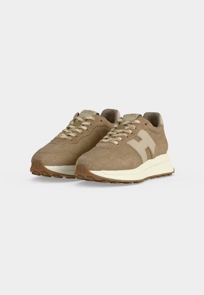Paire de baskets en daim beige avec des accents crème, des lacets et des semelles blanches épaisses sur un fond uni gris clair.