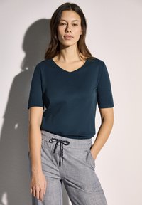 Námorně modré tričko s výstřihem do V vyrobené z bavlněné směsi, kombinované se světle šedými kalhotami na stažení v pase, které mají texturovaný povrch a přední kapsy.