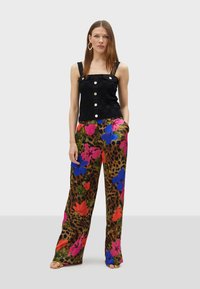 Zwarte cropped top met vierkante halslijn en textuurpatroon, gecombineerd met kleurrijke palazzo broeken met bloemen- en luipaardprint. Platte sandalen.
