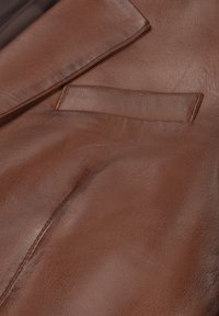 Veste en cuir marron avec une finition texturée, dotée d'un revers pointu et d'une poche poitrine, mettant en valeur son matériau lisse et durable.