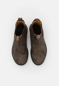 Bottes de cheville en cuir marron avec panneaux élastiques, tige texturée et accents beige contrastants. Présente une boucle pour un enfilage facile. Semelle en caoutchouc plate.