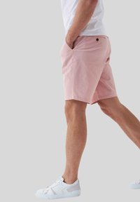 Pantalones cortos rosa claro de corte ajustado, fabricados en un tejido ligero. Cuentan con bolsillos laterales y un bolsillo trasero con un pequeño detalle de botón.