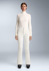 Witte, aansluitende coltrui met geribbelde textuur, gecombineerd met hoge, witte flared broek met twee voorzakken en knoopsluiting.