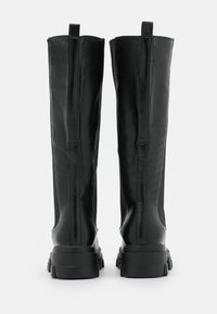 Botas de cuero negro hasta la rodilla con una textura suave, que cuentan con una gruesa suela de goma, un diseño ajustado y tiradores traseros para facilitar su colocación.