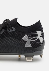 Scarpa da calcio sintetica nera con tomaia testurizzata, caratterizzata da un logo argento e lacci neri. La suola ha tacchetti trasparenti per una migliore aderenza.