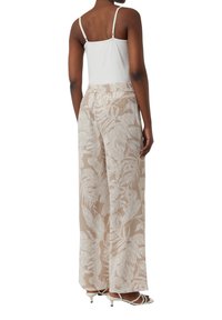 Witte tanktop met dunne banden, gecombineerd met losse, beige wijde broek met een botanische print en elastische tailleband.