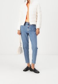 Witte pufferjas, oranje gebreide trui, blauwe rechte jeans, zwarte instapschoenen en een kleine beige handtas. Eenvoudig ontwerp, casual stijl.