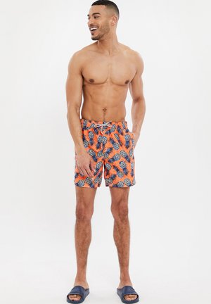 Zwemshorts met een oranje achtergrond, bedrukt met blauwe ananas. Voorzien van een elastische tailleband en een trekkoord.
