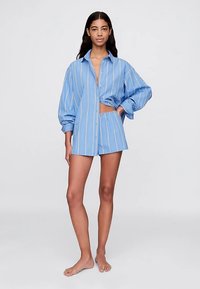 Světle modrá pruhovaná bavlněná košile s oversize střihem, knoflíkovým uzavřením a výřezem. Spárováno s odpovídajícími šortkami z podobného materiálu.