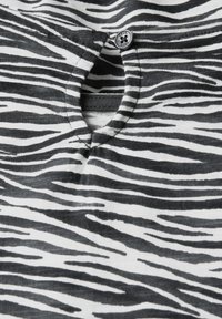 Schwarz-weiß gestrefter Stoff mit Zebrastreifen, featuring einen Ausschnitt und einem Knopf mit der Aufschrift "CECIL". Weiche Textur, lässiges Design.