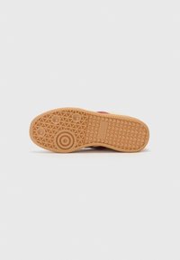 Gum rubber outsole with a textured herringbone pattern, featuring circular and oval traction points, and embossed logo detail.