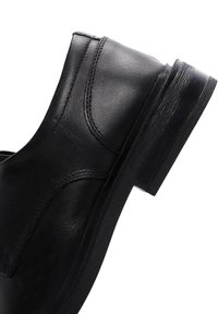 Bottine en cuir noir avec une texture lisse, des détails de couture courbés et un petit talon robuste pour la stabilité.