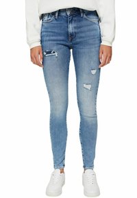 Jeans ajustados en denim azul claro con desgastes en las rodillas, una cintura alta y una textura suave. Combinados con zapatillas blancas.