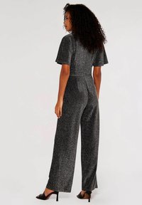 Glanzende zwarte jumpsuit met korte vlinder mouwen, wijde benen en een getailleerde taille. Gladde textuur met minimale accenten.