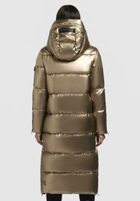 Langer, fluffiger goldener Parka mit einer großen Kapuze, der genähte Abschnitte, eine glatte Textur und ein Logotag auf der Rückseite aufweist. Enthält seitliche Reißverschlüsse.