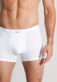 Weisse Baumwoll-Boxershorts mit engem Schnitt, elastischem Bund und einem Etikett auf der Rückseite. Glatte Textur und minimalistisches Design.