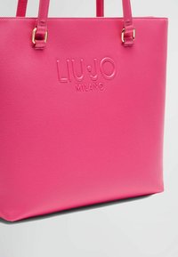 Borsa a tracolla sintetica rosa con logo embossato "LIU·JO MILANO", dotata di manici piatti e superficie testurizzata. Bordo inferiore liscio.