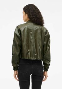 Gecropte grüne Lederbomberjacke mit geripptem Kragen, elastischen Bündchen und glatter Textur, kombiniert mit schwarzen Jeans.