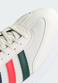 Białe sneakersy z teksturowanej tkaniny, z czerwonymi, zielonymi i granatowymi zygzakowymi paskami. Gumowa podeszwa i sznurowanie zapewniające pewne dopasowanie.