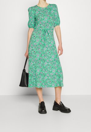 Zelené květinové midi šaty s krátkými nabíranými rukávy, měkkou látkou a stahovaným pasem. Kombinované s černými mokasínami a černou kabelkou.